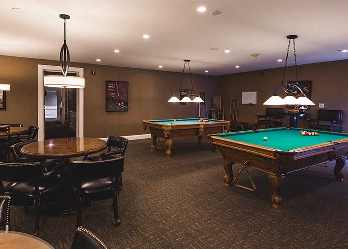 A cozy billiard room featuring two pool tables under stylish lighting.