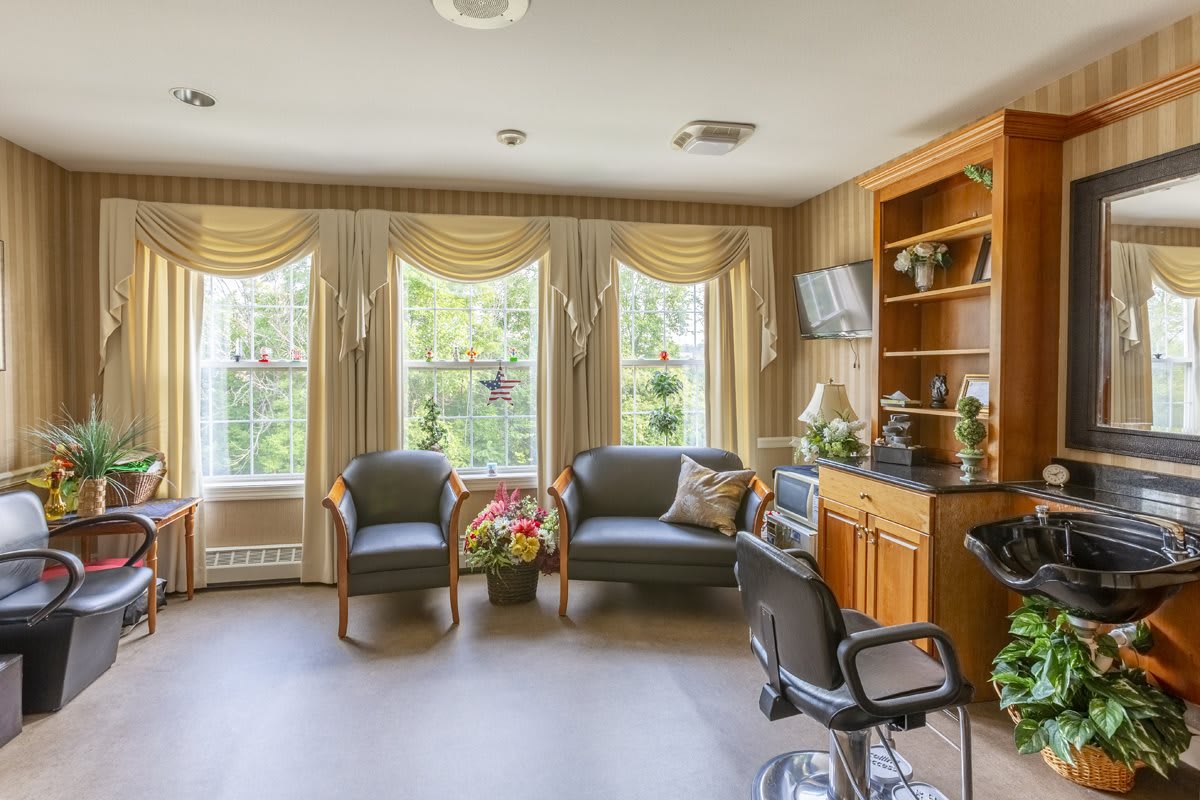 A cozy waiting room with comfortable chairs and large windows adorned with curtains, featuring wooden bookshelves and a television.