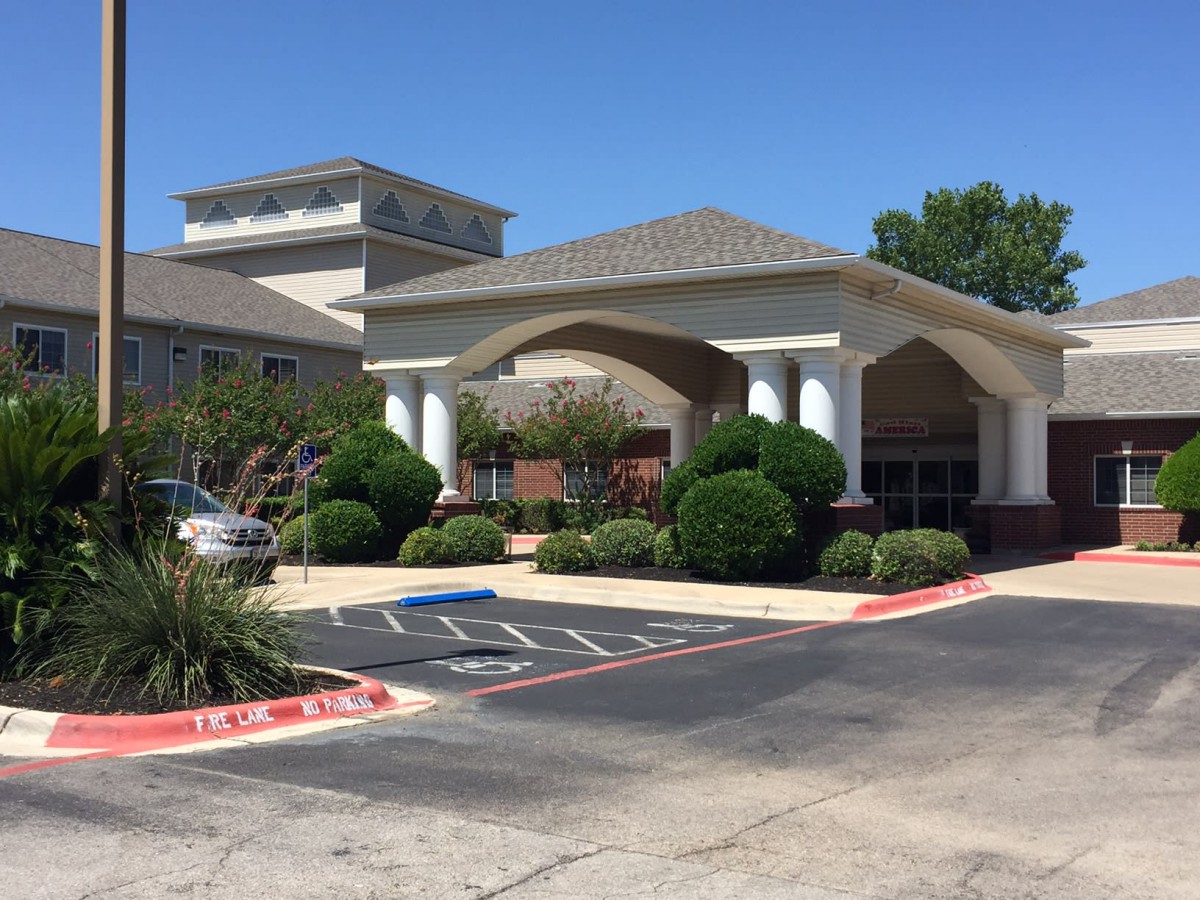 A building entrance with a landscaped area and parking lot during daytime.