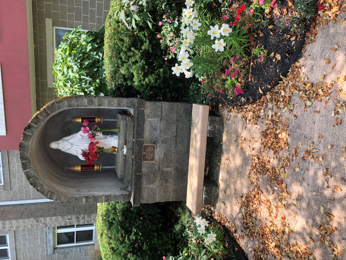 A small garden shrine with a statue surrounded by colorful flowers and greenery.