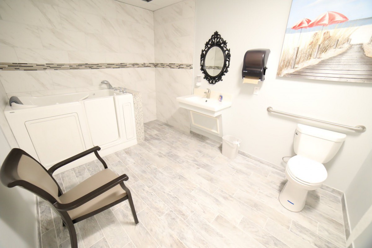 A spacious and elegantly designed bathroom with a chair, ornate mirror, sink, and tiled flooring.
