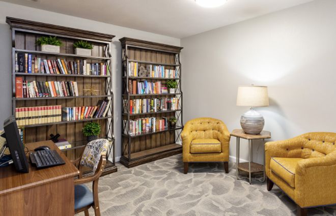 A cozy reading room with bookshelves, armchairs, and a lamp.