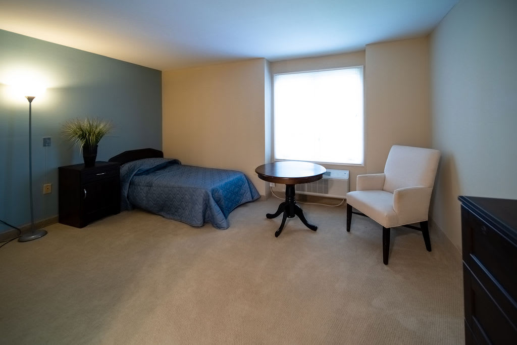 A minimalist bedroom featuring a single bed, a table, and a chair near a window.