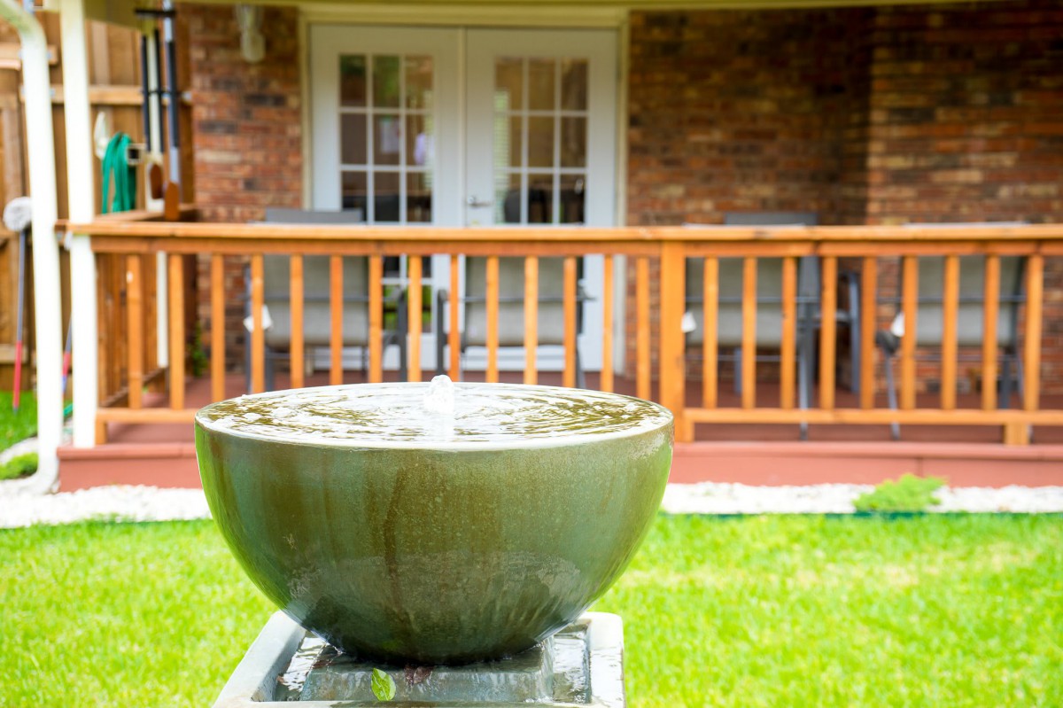 A tranquil garden fountain in a backyard setting with a wooden deck.