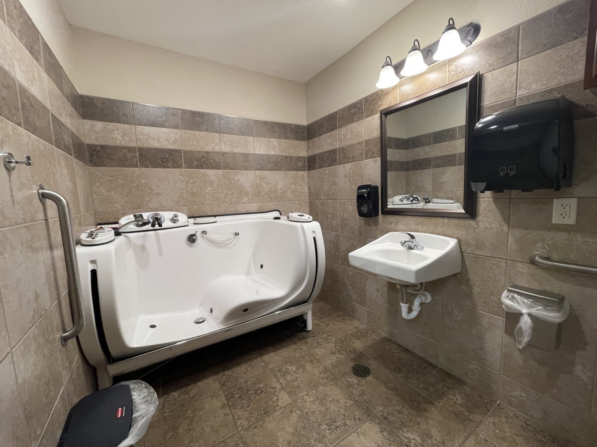 A modern bathroom with a bathtub, sink, and mirror, featuring tiled walls and floor.