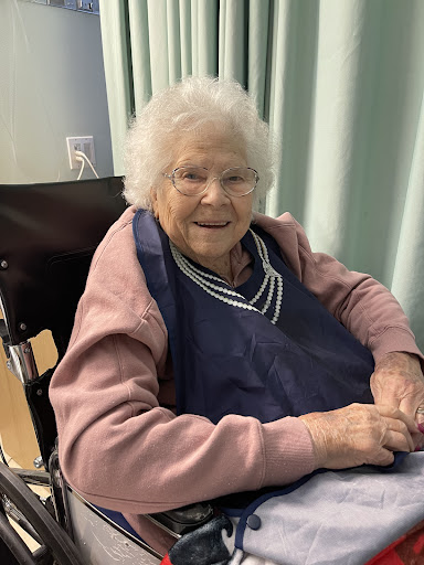 An elderly woman smiling warmly while seated in a wheelchair.