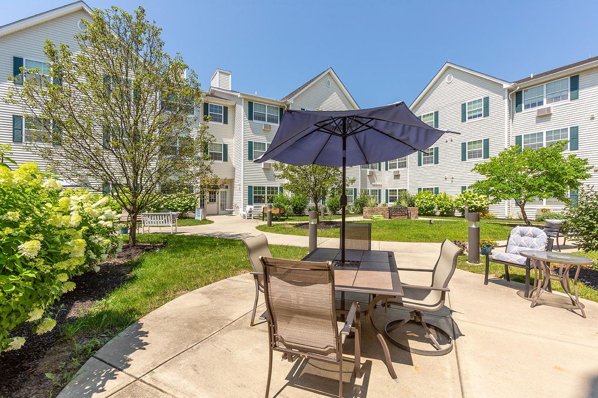 Sunny outdoor patio area with furniture and umbrella in an apartment complex.