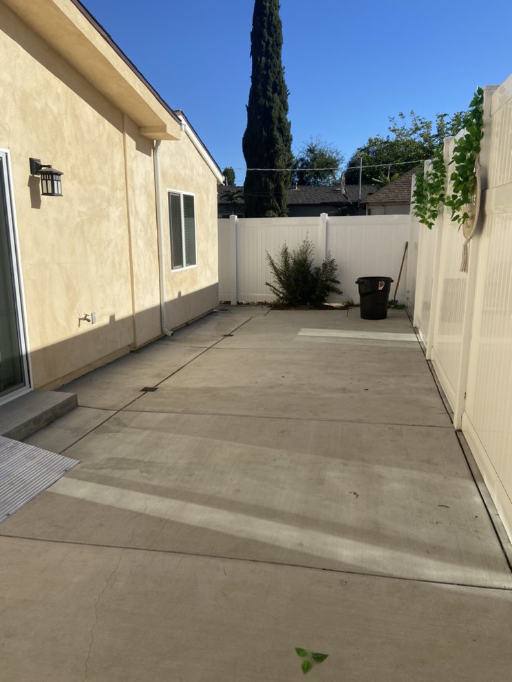 A sunny backyard with a concrete patio and surrounding fence.
