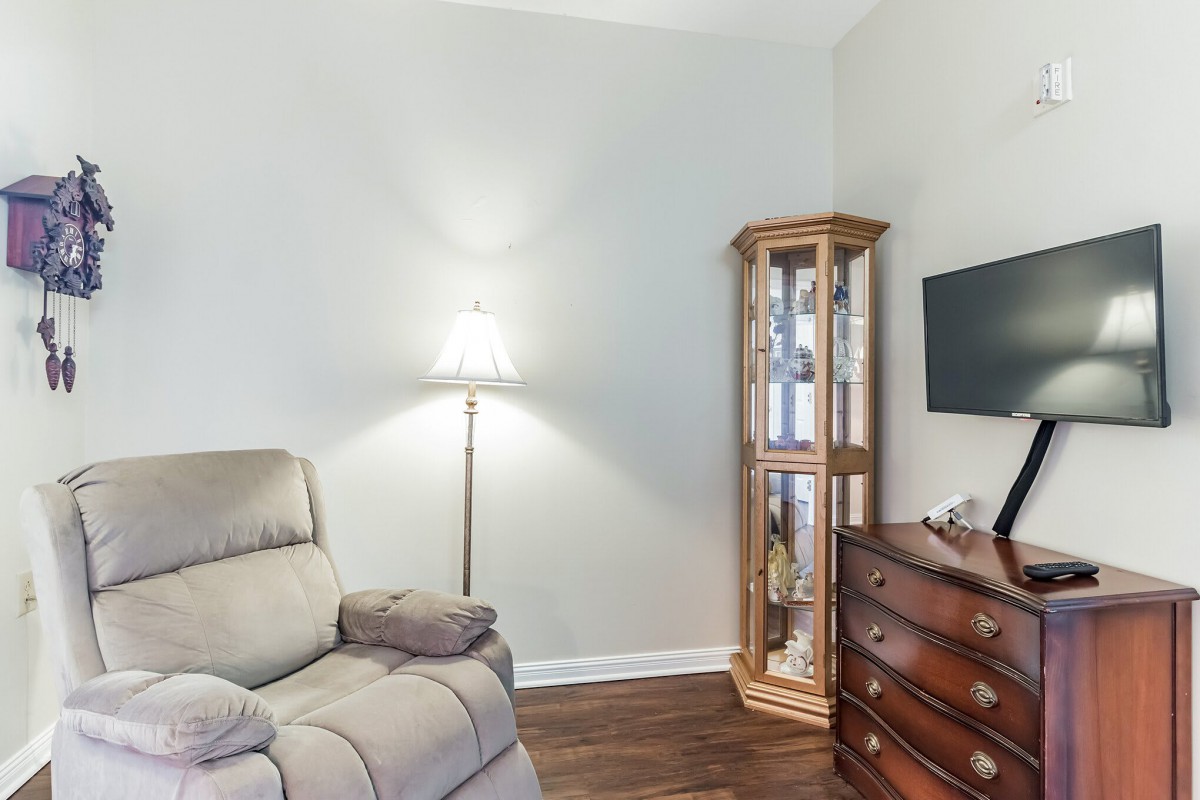 A cozy living room corner with an armchair, a lamp, a wooden cabinet, and a mounted television.