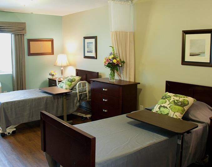 A shared nursing home room with two hospital beds and comfortable furnishings.
