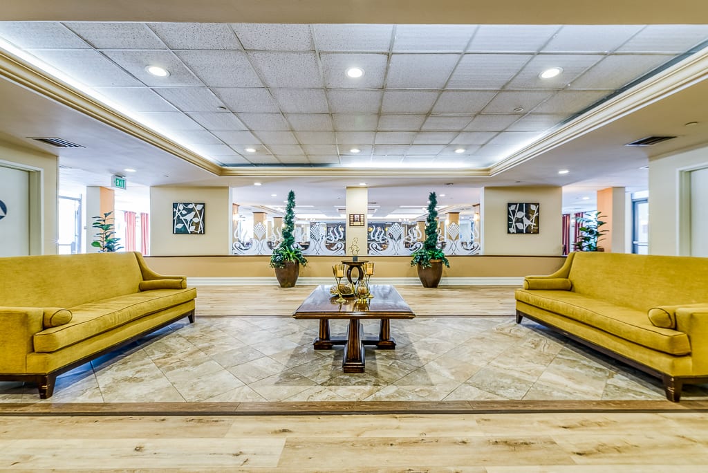 A spacious lobby with elegant interior design, featuring comfortable seating, decorative plants, and ceiling lighting.