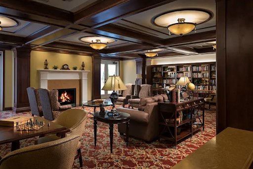 A cozy lounge area featuring comfortable seating, a warm fireplace, and bookshelves filled with books.