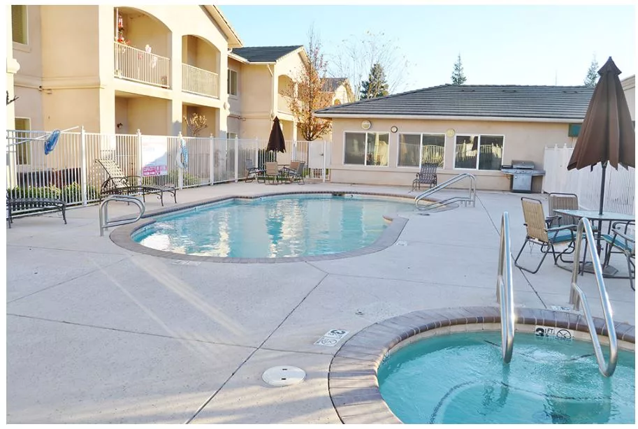 A serene outdoor swimming pool and jacuzzi at an apartment complex on a sunny day.