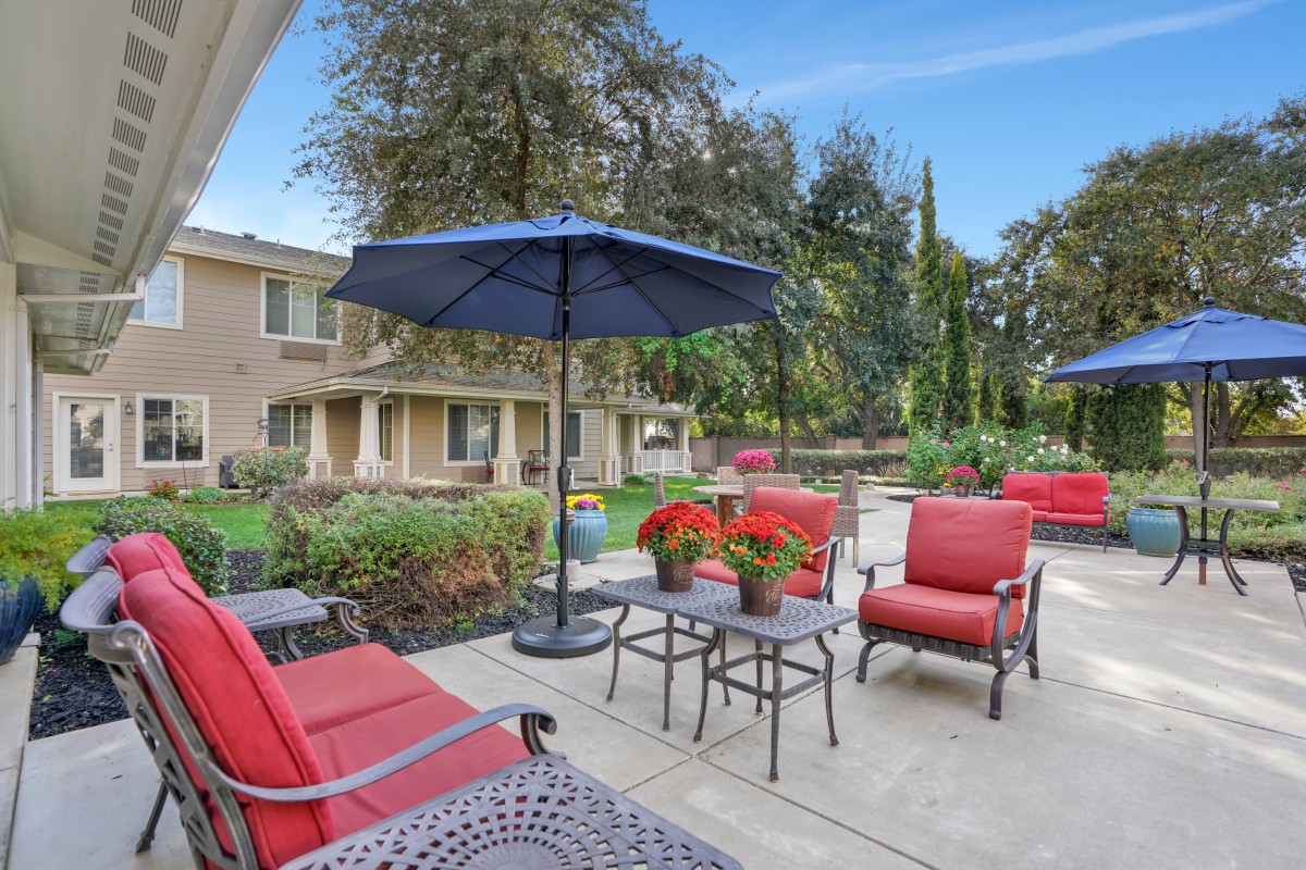 A cozy outdoor patio with comfortable seating and a large umbrella, surrounded by greenery.