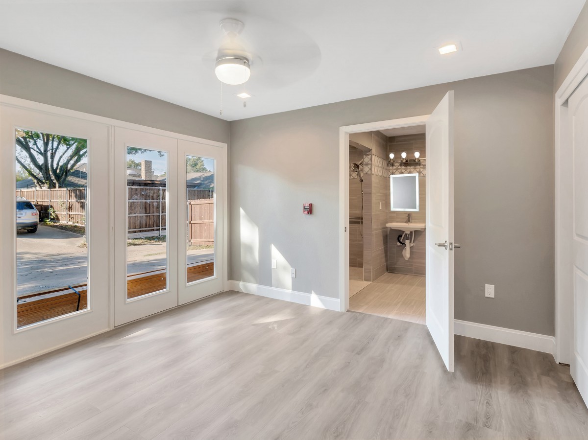 A modern, empty bedroom with wooden flooring and French doors leading to the outside.
