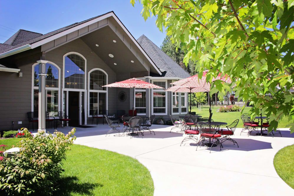 A beautiful house with a spacious outdoor patio, featuring tables, chairs, and umbrellas on a sunny day.