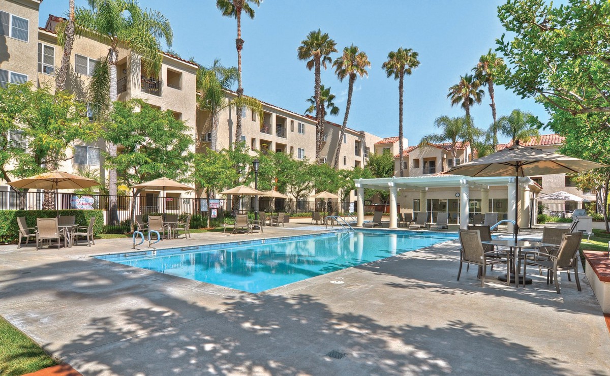 A serene outdoor swimming pool surrounded by a residential complex with tall palm trees.