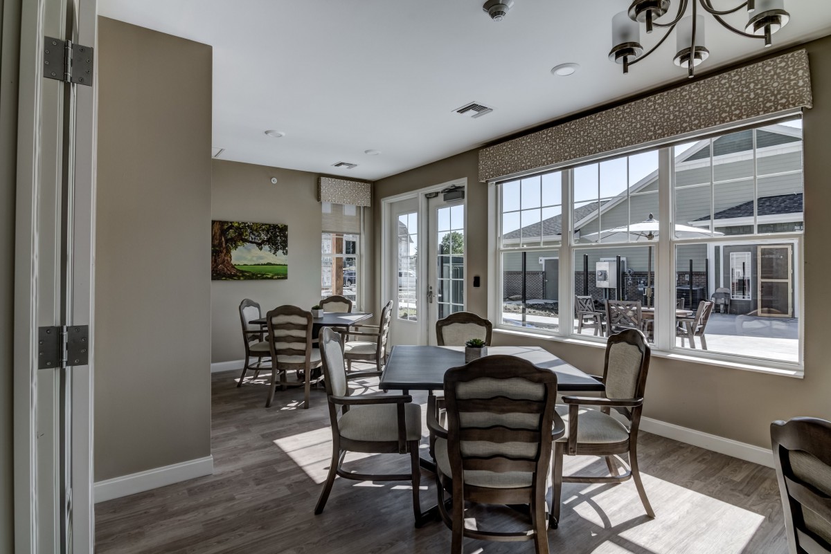 A modern dining area with tables and chairs, illuminated by natural sunlight through large windows.