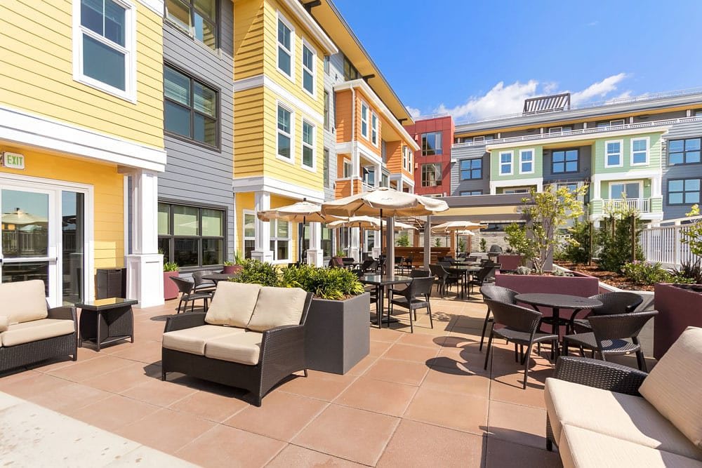A sunny patio area with comfortable seating and umbrellas at a modern apartment complex.