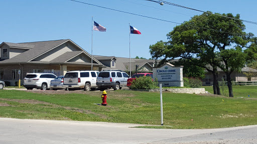 A facility in Texas with American and state flags flying, surrounded by vehicles and green grass.