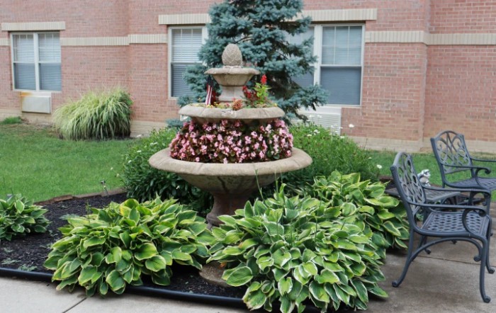 A decorative garden fountain surrounded by vibrant flowers and lush hosta plants.