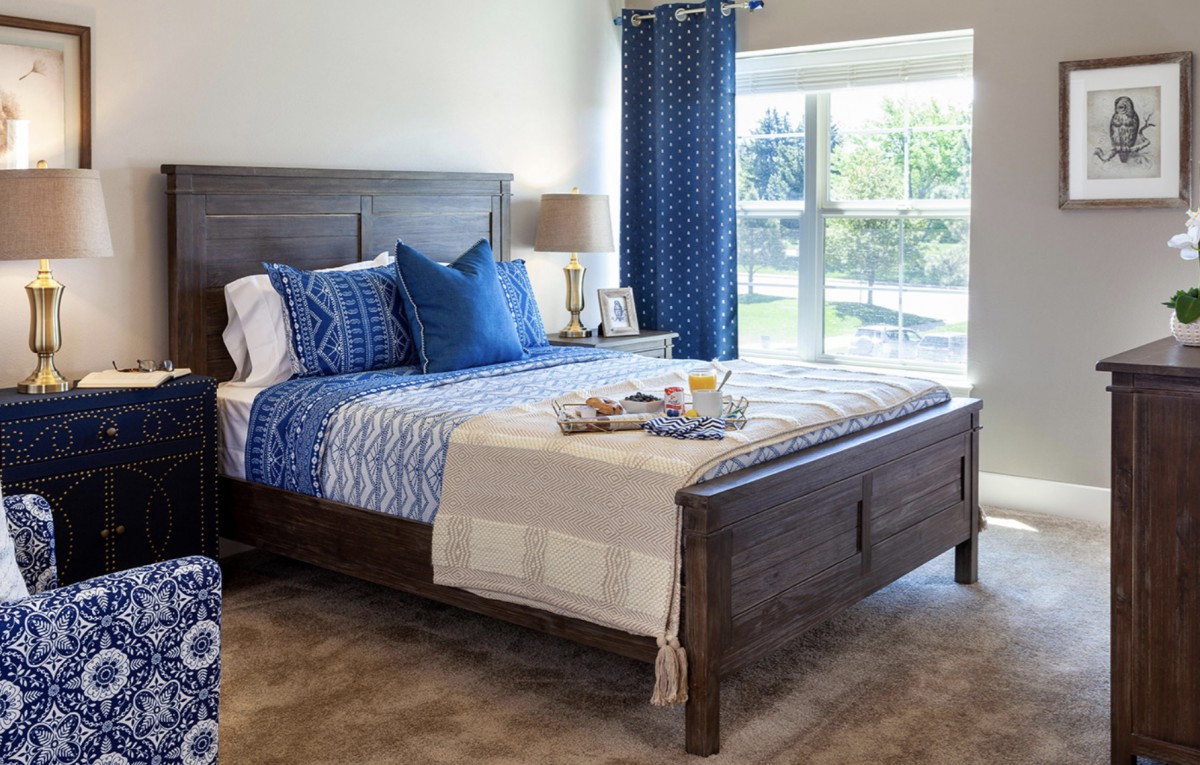 A cozy bedroom with a wooden bed, blue accents, and a large window.