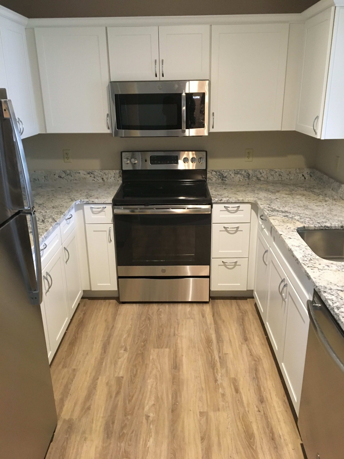 A modern kitchen with stainless steel appliances, white cabinets, granite countertops, and hardwood flooring.