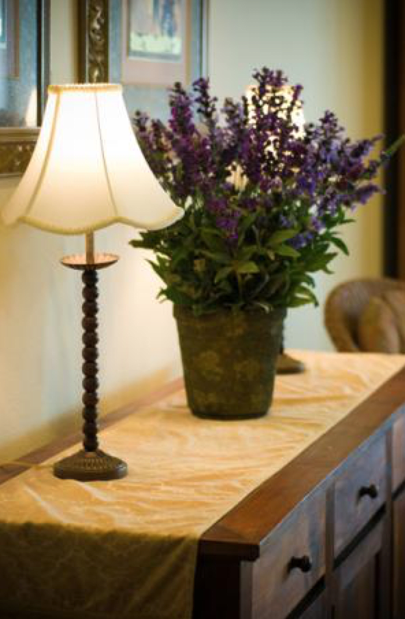 A decorative table setup featuring a table lamp and a potted plant with purple flowers.
