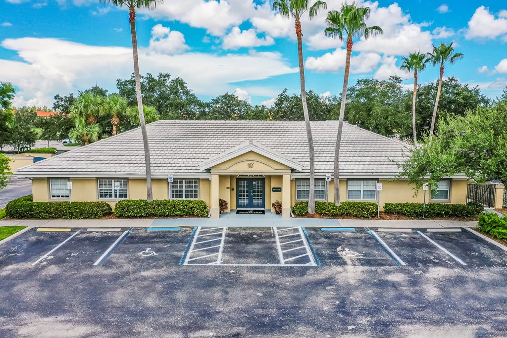 A single-story building with a parking lot and palm trees under a sunny sky.