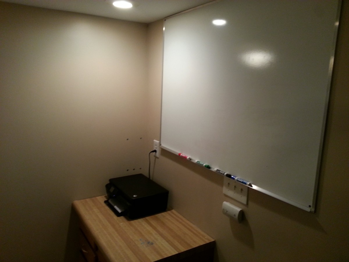A small office workspace with a whiteboard, printer, and desk.