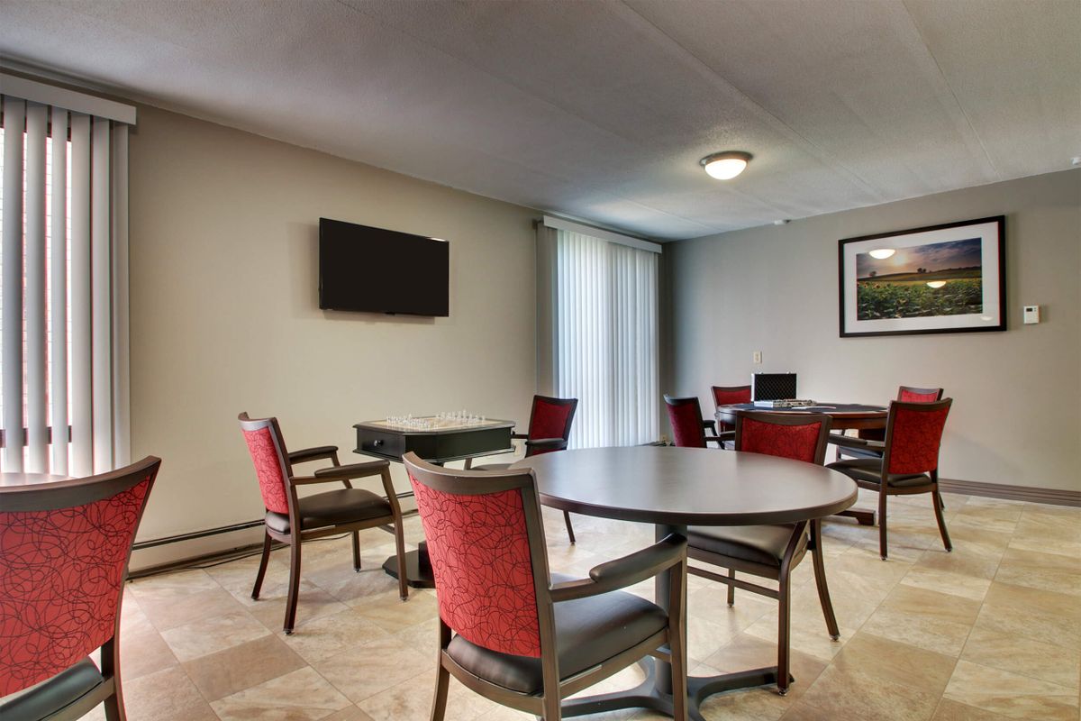 A meeting room with multiple tables and chairs, featuring a wall-mounted television.
