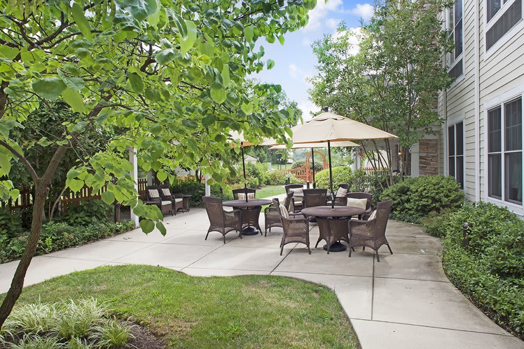 A peaceful outdoor patio area with tables, chairs, and umbrellas surrounded by lush garden landscaping.