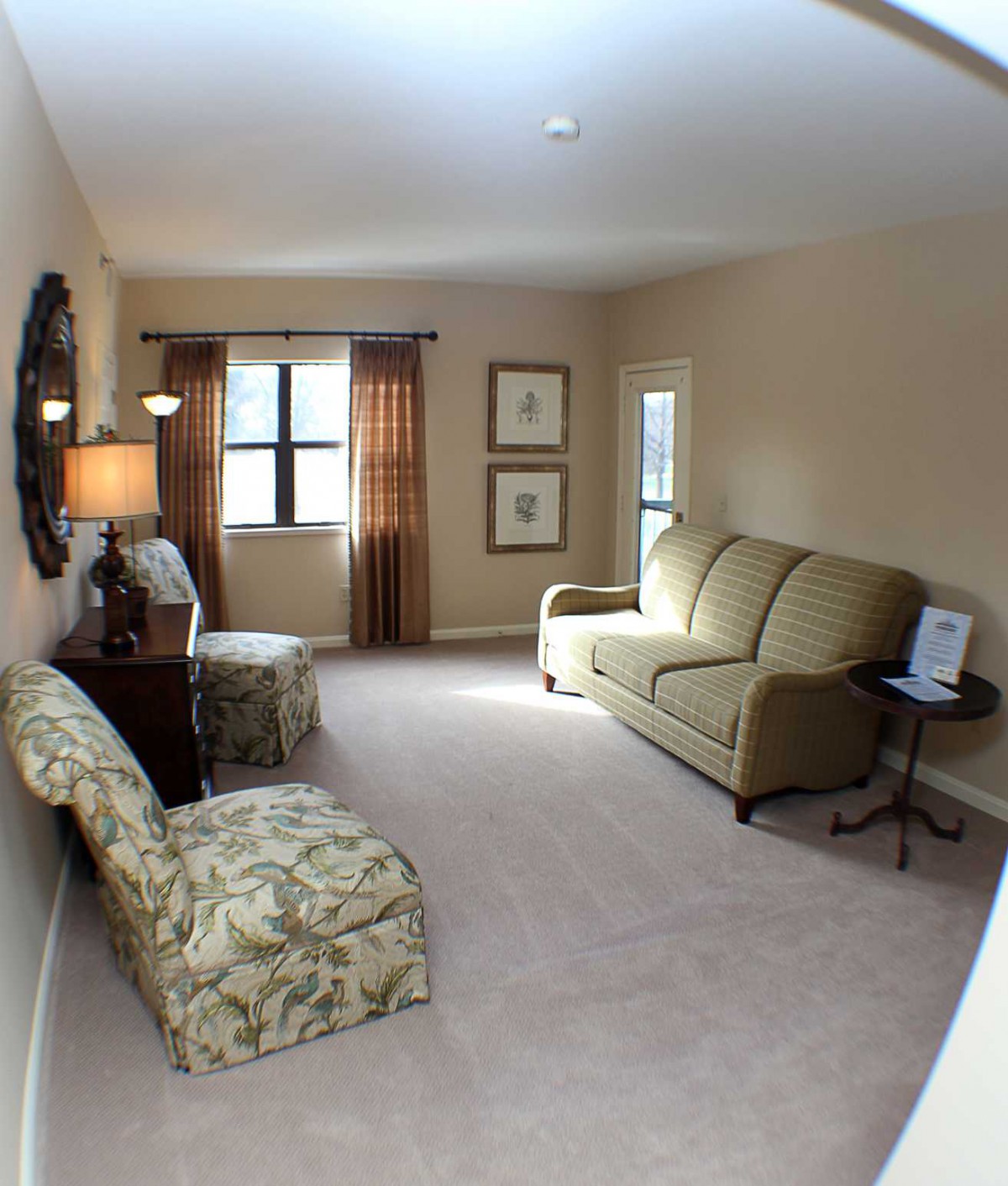 A cozy living room with a sofa, floral chairs, and warm lighting.