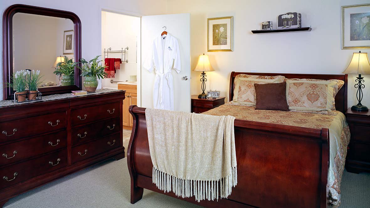 A cozy bedroom with a wooden bed frame, dresser, and ambient lighting.