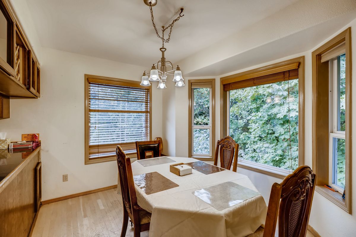 A cozy dining room with a chandelier, surrounded by large windows and featuring a table set for four.