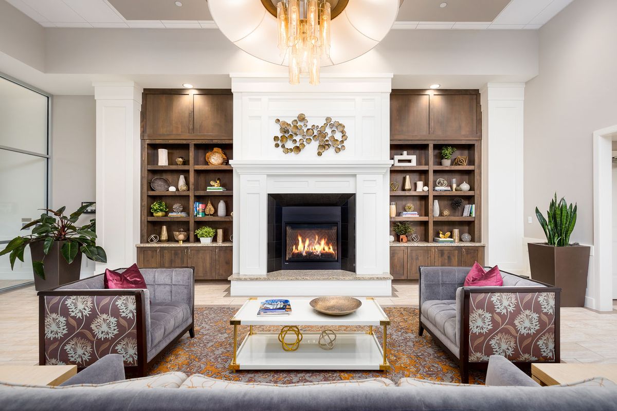 A modern living room features a central fireplace, flanked by built-in shelves, comfortable sofas, and a stylish coffee table under a striking chandelier.