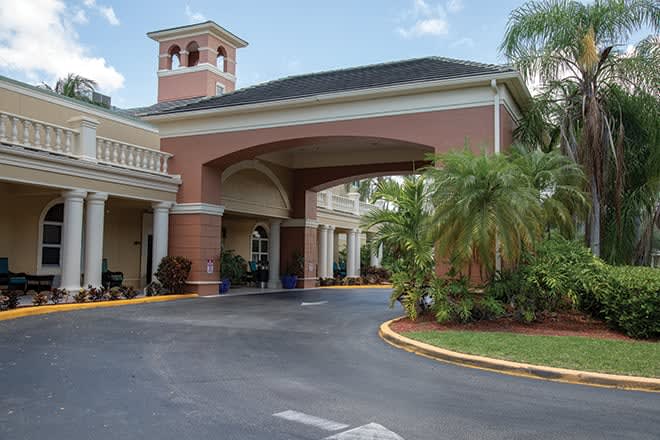 A building entrance with an archway and palm trees lining the driveway.