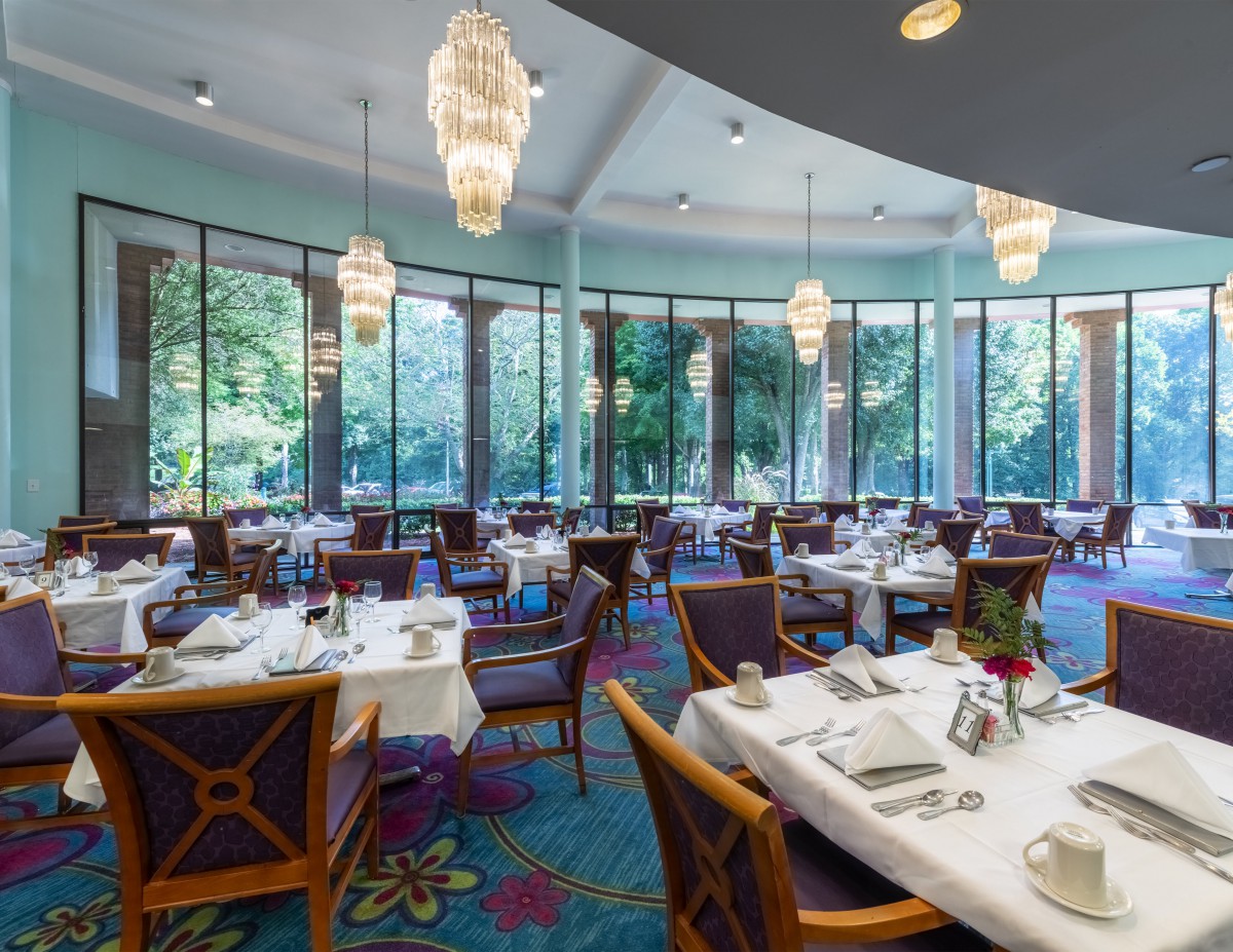 An elegant dining room with beautifully set tables and large windows overlooking the greenery.