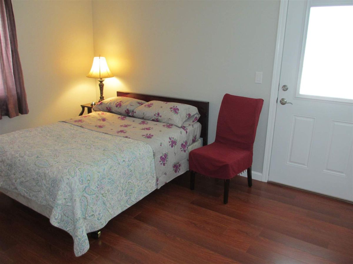 A simple bedroom with a bed, lamp, and chair on a wooden floor.