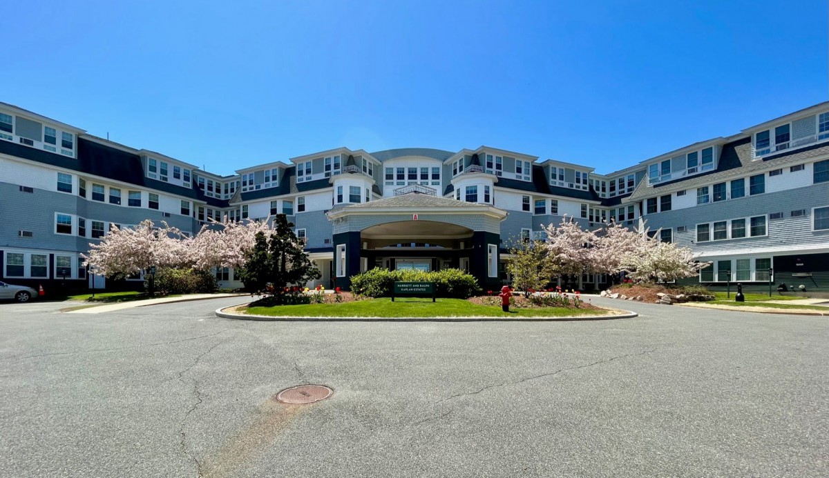 A large, multi-story hotel with a grand entrance surrounded by blooming trees against a clear blue sky.
