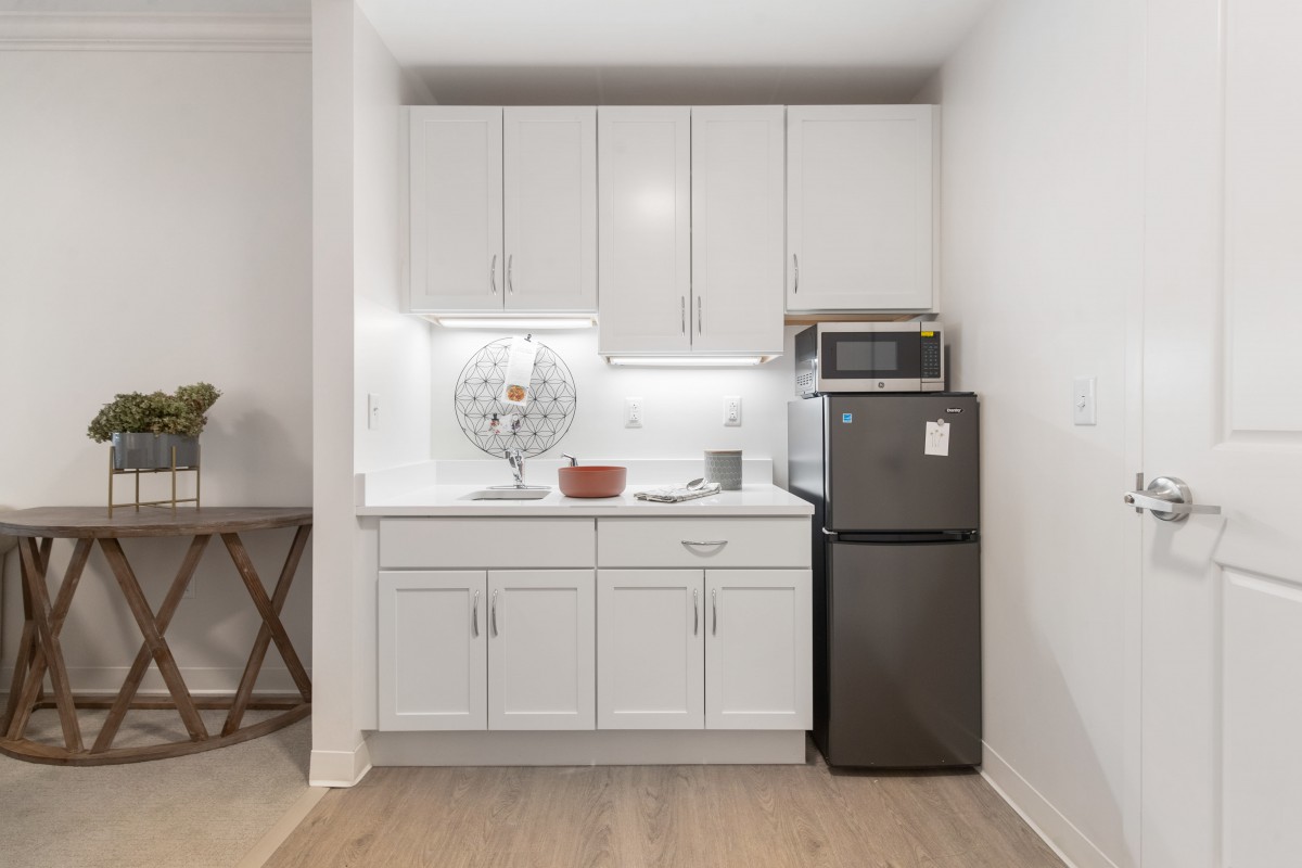 A compact modern kitchen with white cabinetry, a microwave, and a small refrigerator.
