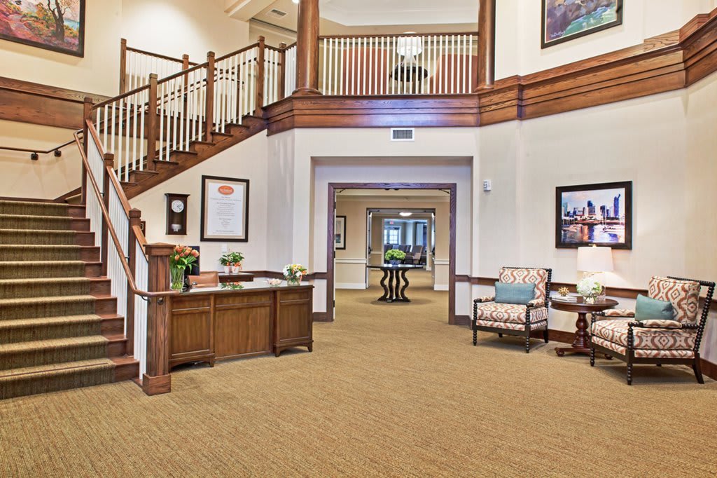 A spacious lobby with a reception desk, seating area, and wooden staircase.