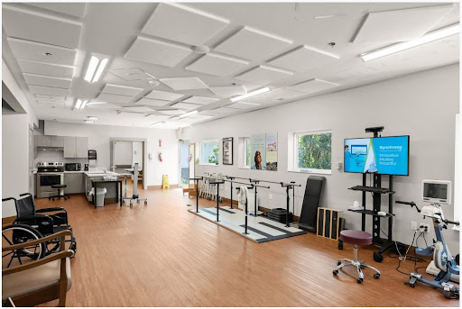 A well-equipped rehabilitation therapy room with exercise equipment and ample natural light.