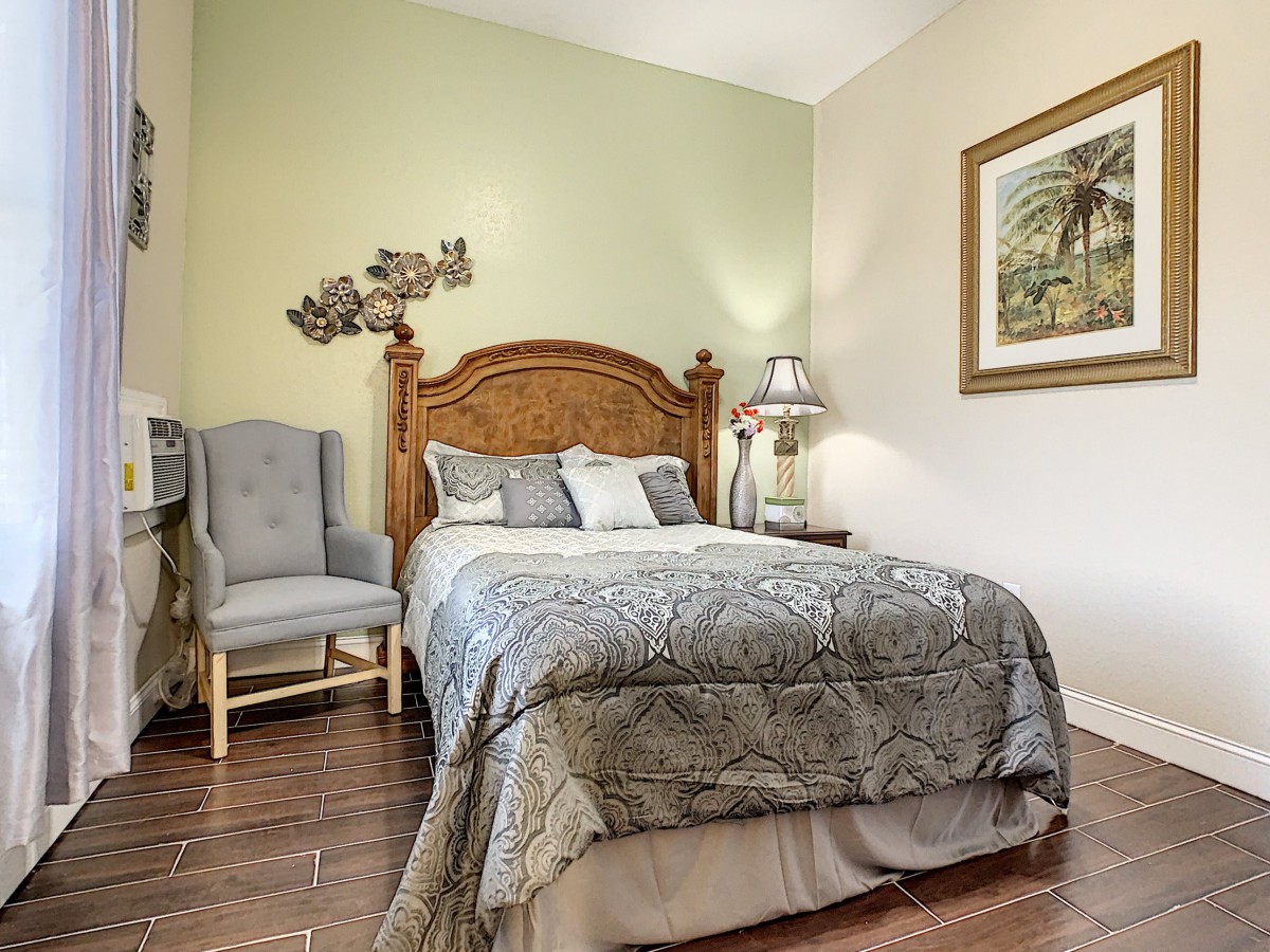 A cozy bedroom with a wooden headboard, elegant bedding, and stylish decor including a chair, lamp, and artwork.