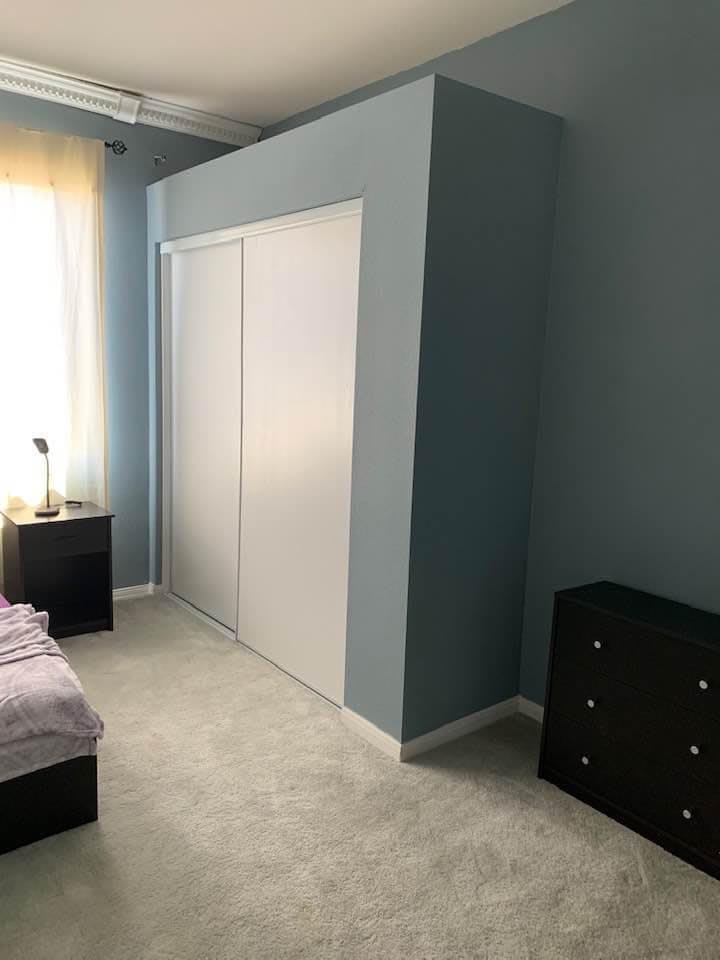 A minimalist bedroom with a bed, nightstand, dresser, and a sliding closet door.