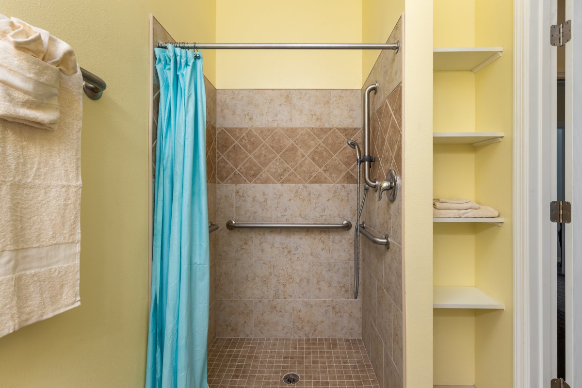 A shower area with a blue curtain, tiled walls, and grab bars for safety.