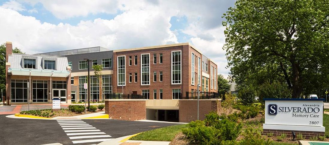 A modern brick building featuring large windows and a parking garage entrance beneath, set against a partly cloudy sky.