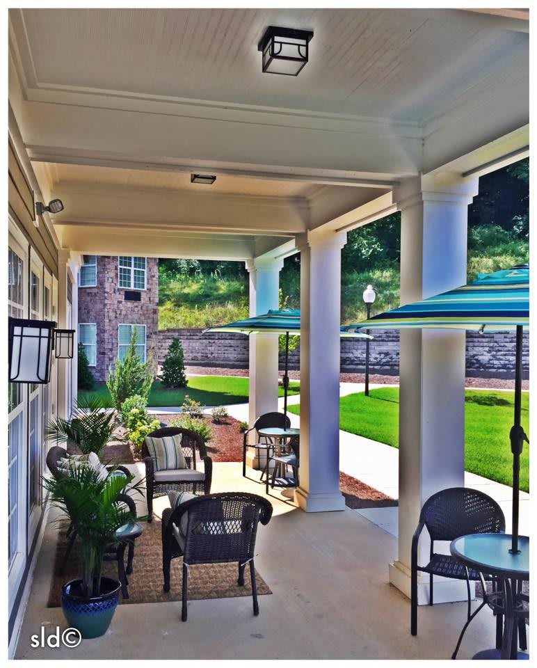 A cozy outdoor patio with seating, tables, and umbrellas overlooking a garden.