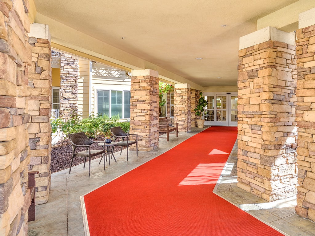 A red carpet leads through a covered entrance with stone columns and outdoor seating.