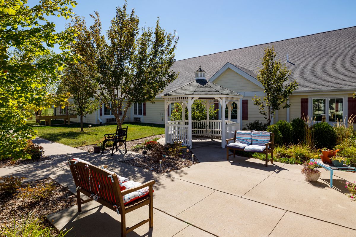 A sunny outdoor patio with a gazebo and benches surrounded by trees.